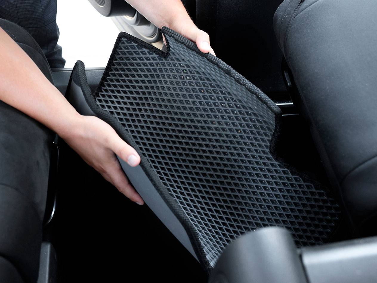 Persoană așezând un covoraș auto negru din cauciuc cu model de diamant într-un vehicul.