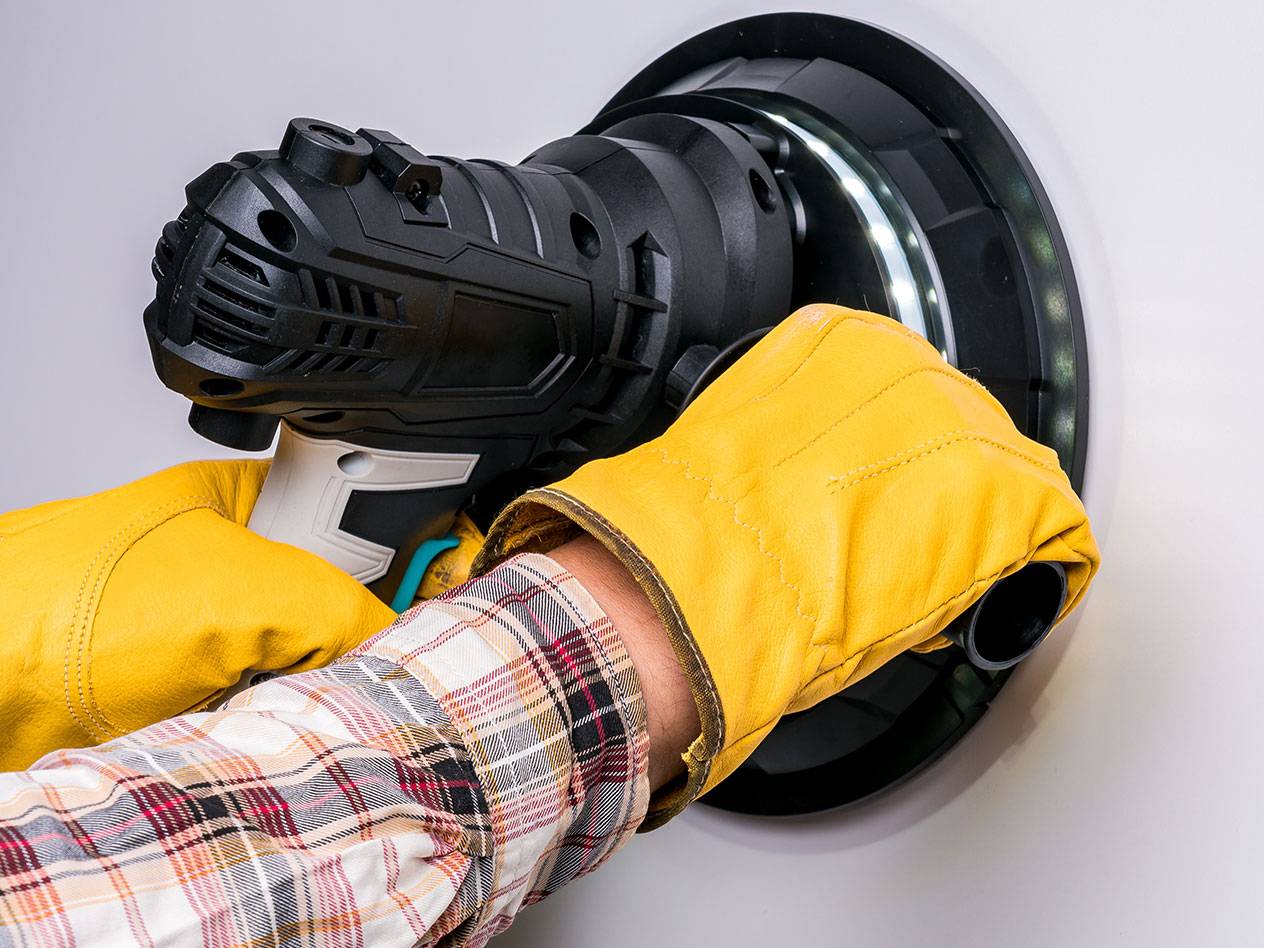 Șlefuitor electric de perete cu lumină LED, utilizat de o persoană cu mănuși.