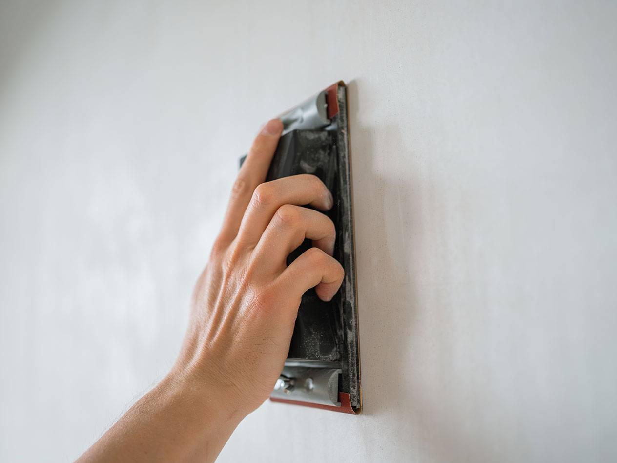 Mână șlefuind un perete cu un bloc de șlefuit