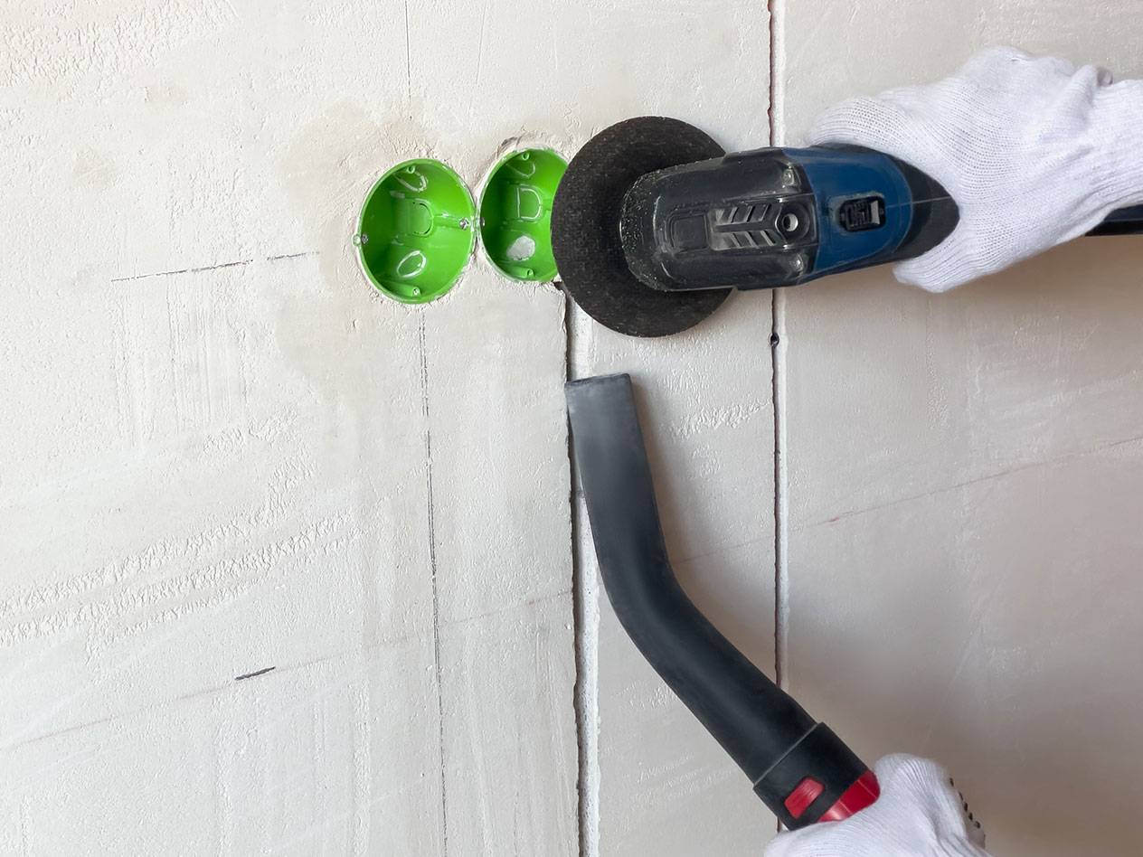 Unealtă electrică tăind șanțuri într-un perete cu un aspirator pentru praf.