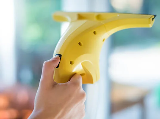 Mână ținând un curățător electric de geamuri galben, curățând o fereastră.