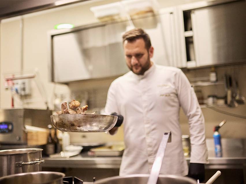 Un bucătar în uniformă albă aruncă mâncare într-o tigaie.