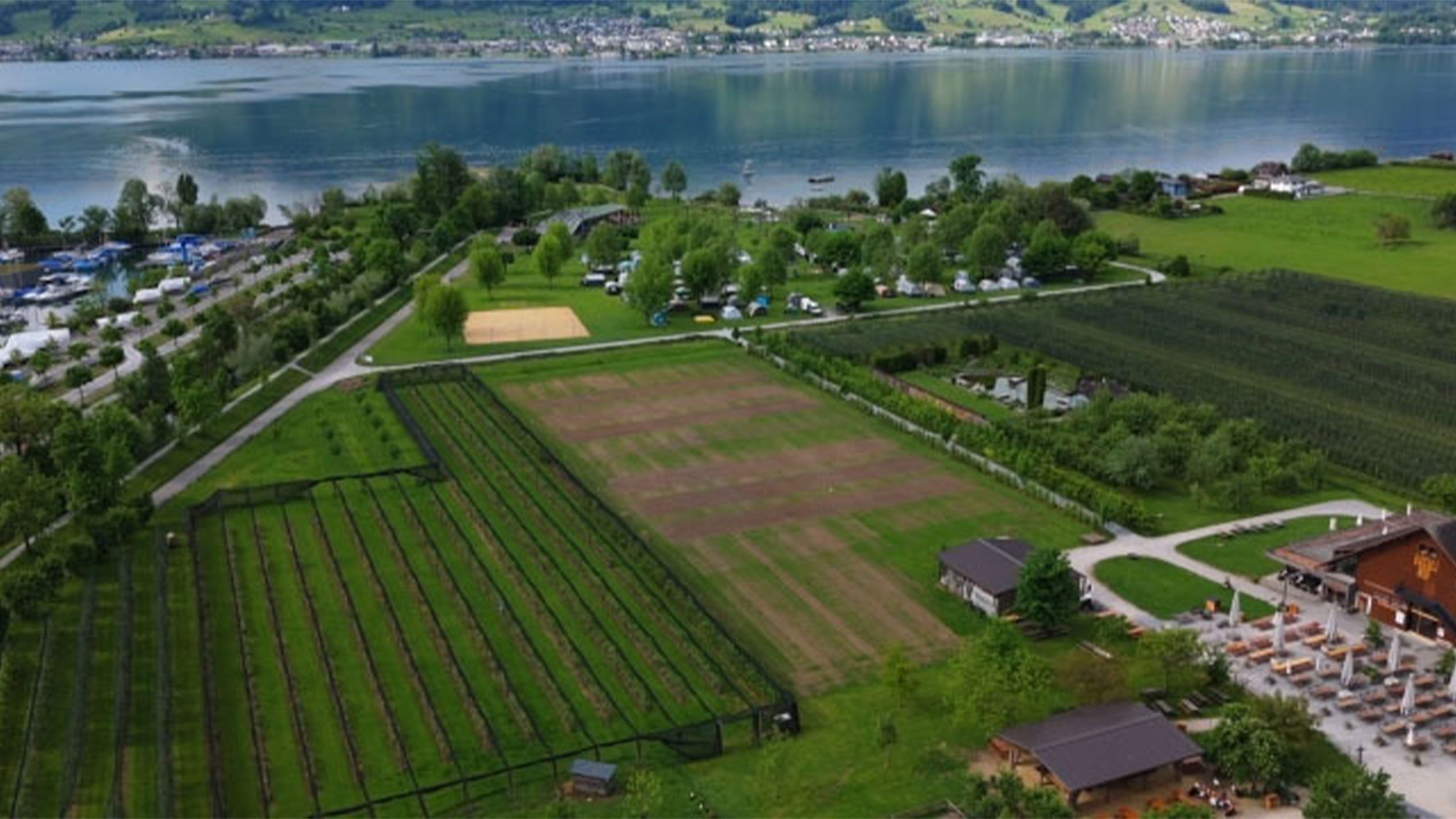 Vedere aeriană a unui camping lângă un lac, cu grădini și un restaurant.