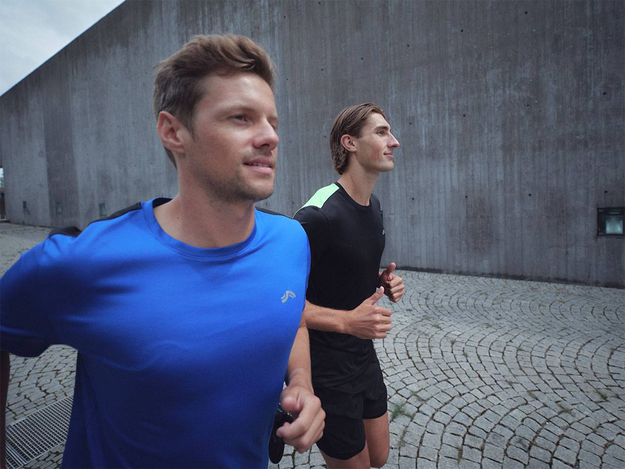 Doi bărbați aleargă în tricouri și pantaloni scurți sport, unul albastru și unul negru.