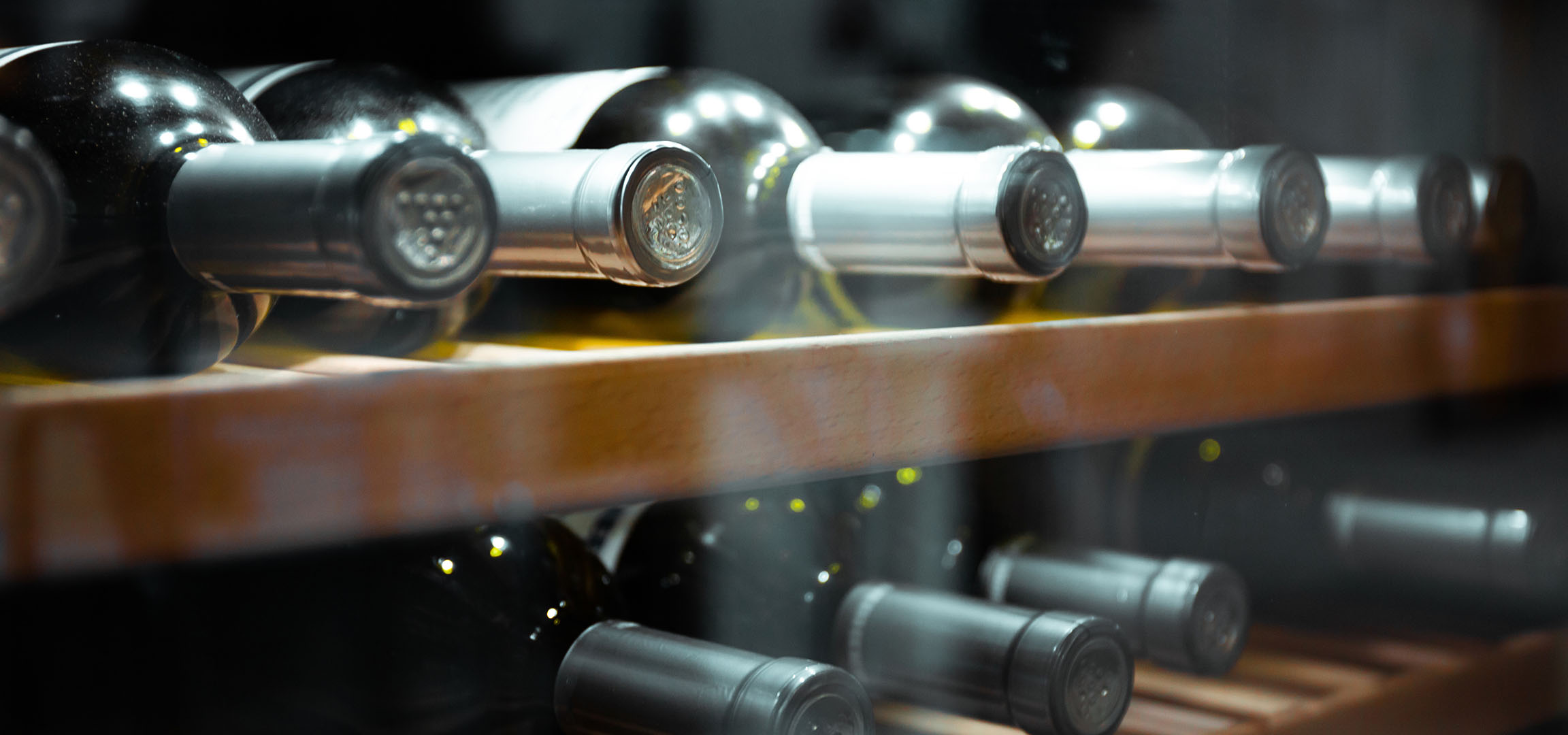 Prim-plan cu sticle de vin pe un raft de lemn, arătând capacele și reflexiile lor.