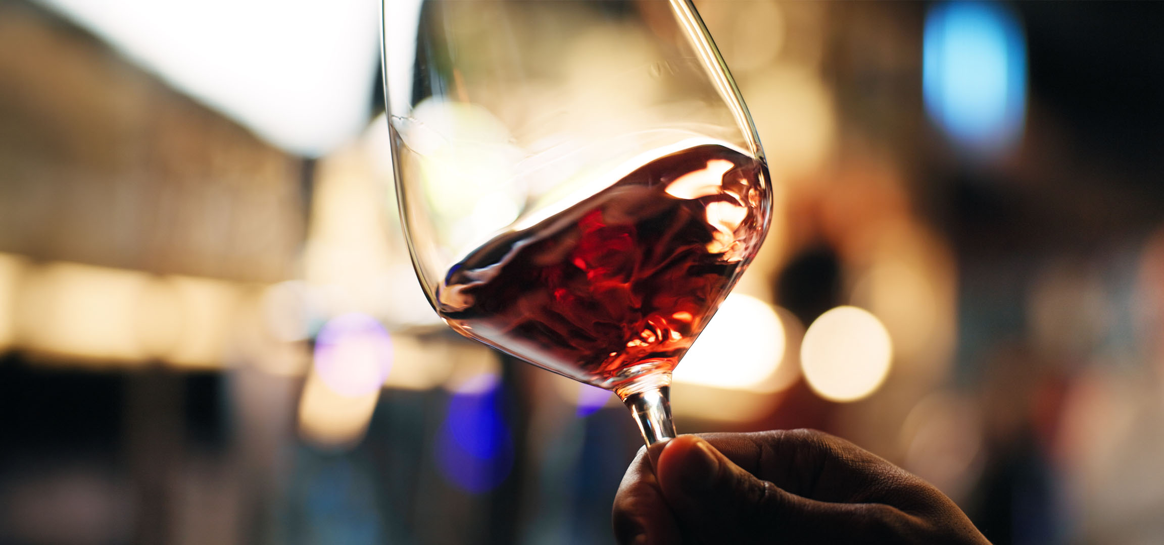 Prim-plan cu un pahar de vin roșu cu lumini estompate în fundal.