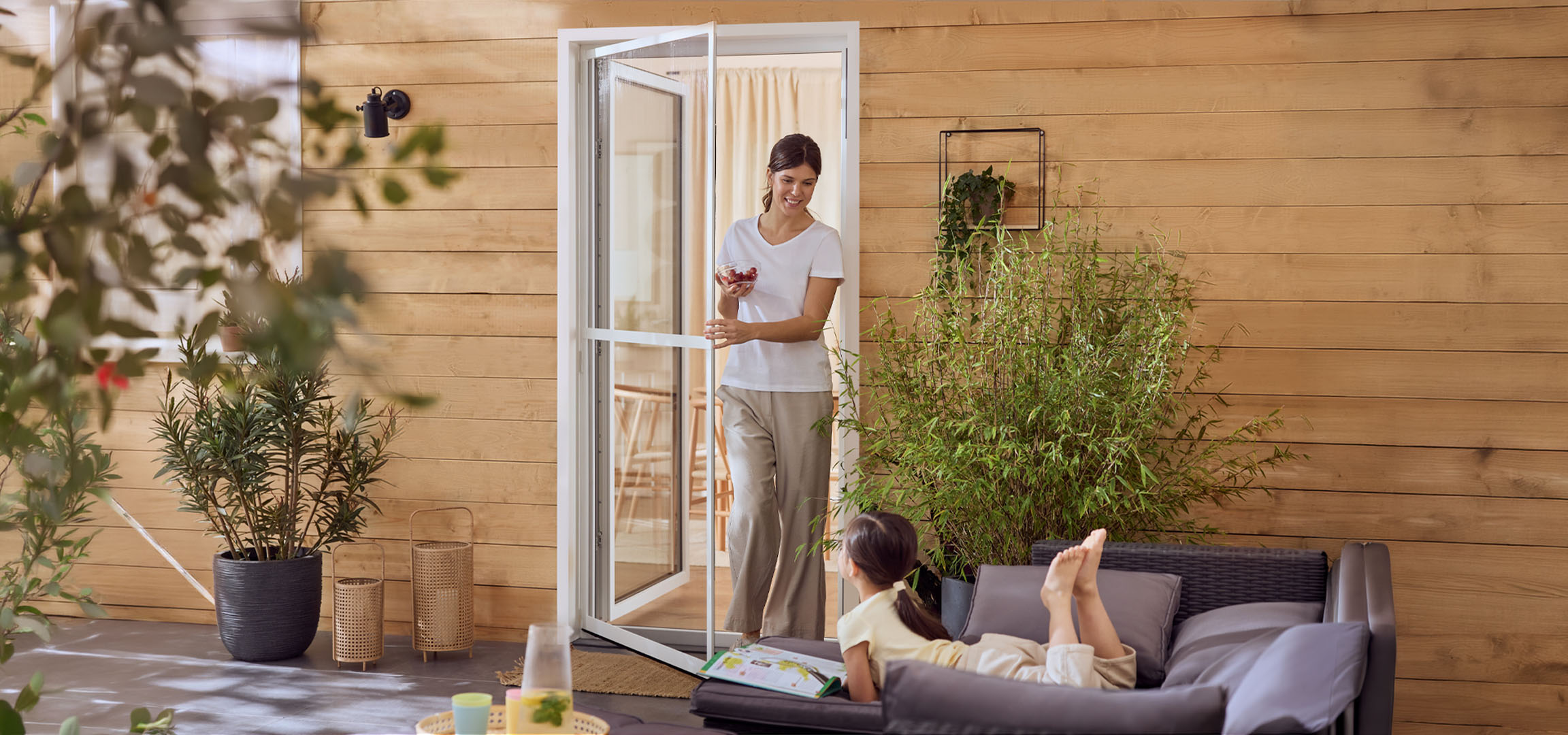 Femeie și fată bucurându-se de o terasă cu mobilier de exterior și plante.