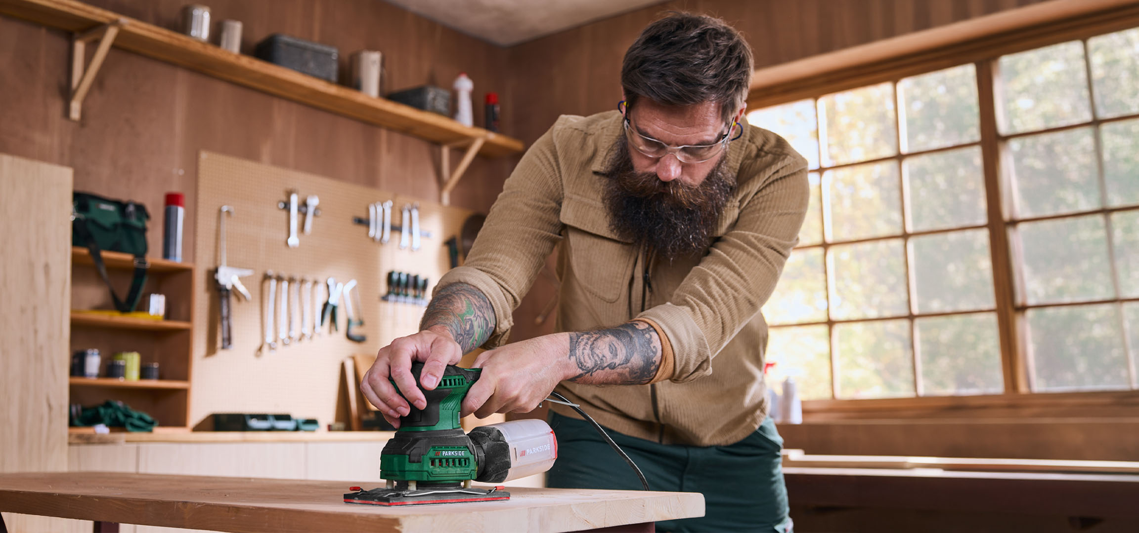 Un bărbat șlefuiește o scândură de lemn cu un șlefuitor electric într-un atelier.