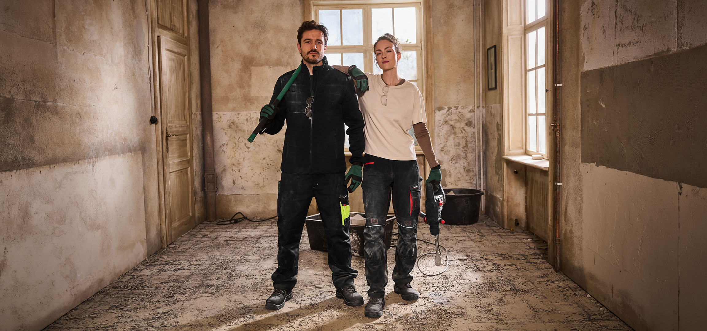 Doi muncitori în construcții în salopete cu unelte pe un șantier.