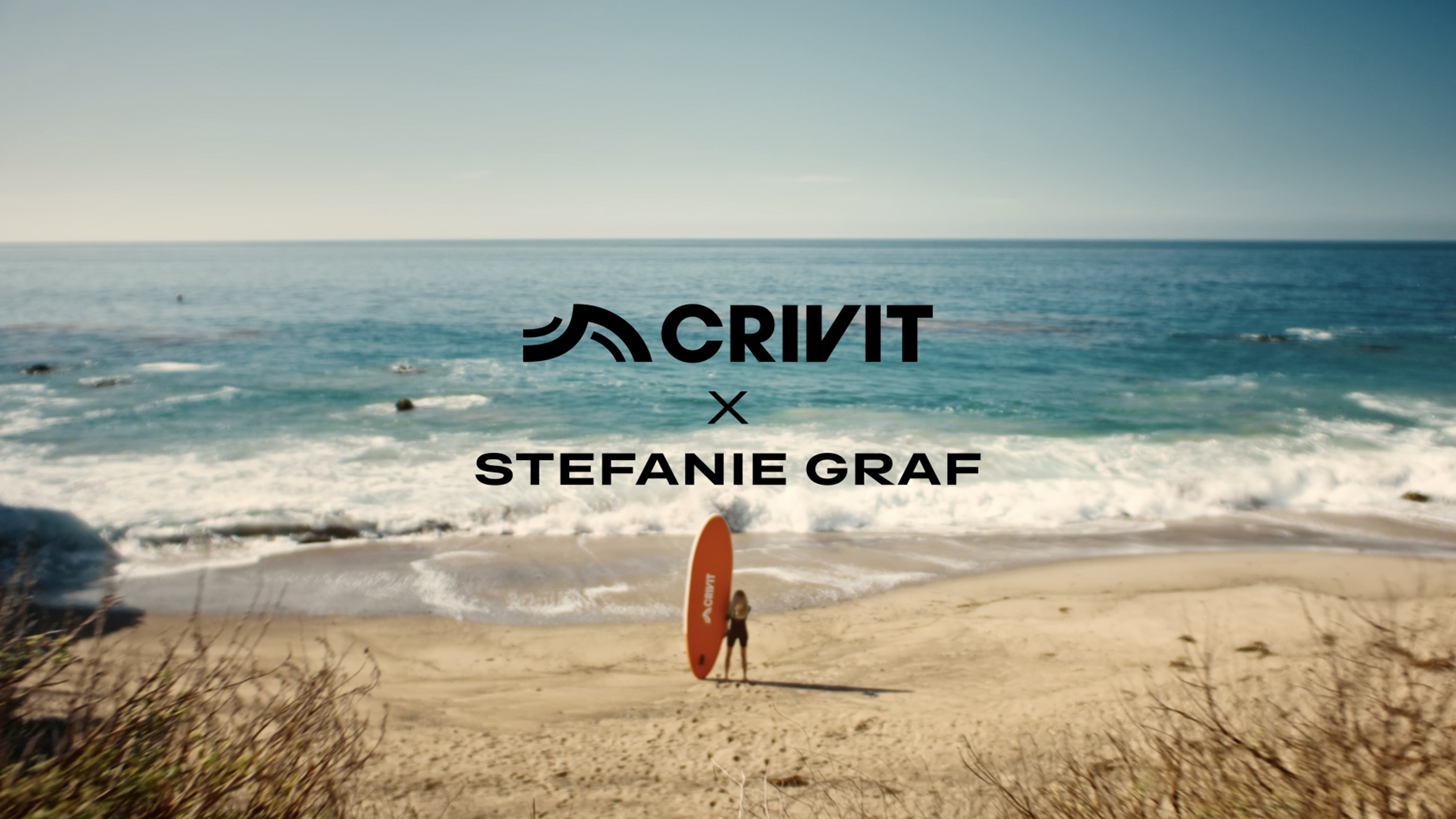 Femeie cu o placă SUP portocalie pe o plajă nisipoasă, cu marea în fundal.