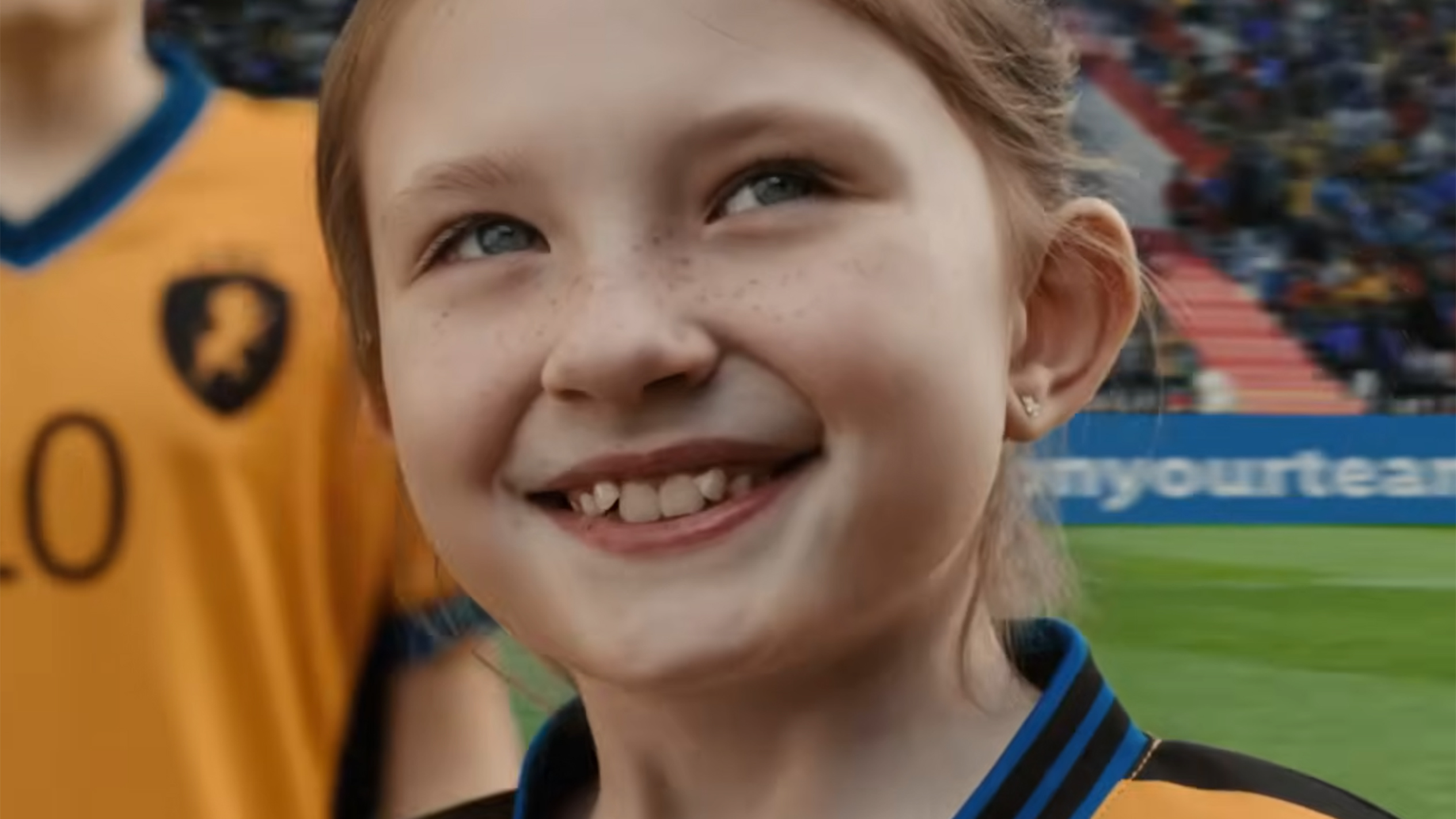 O fetiță cu pistrui zâmbește purtând un tricou de fotbal.