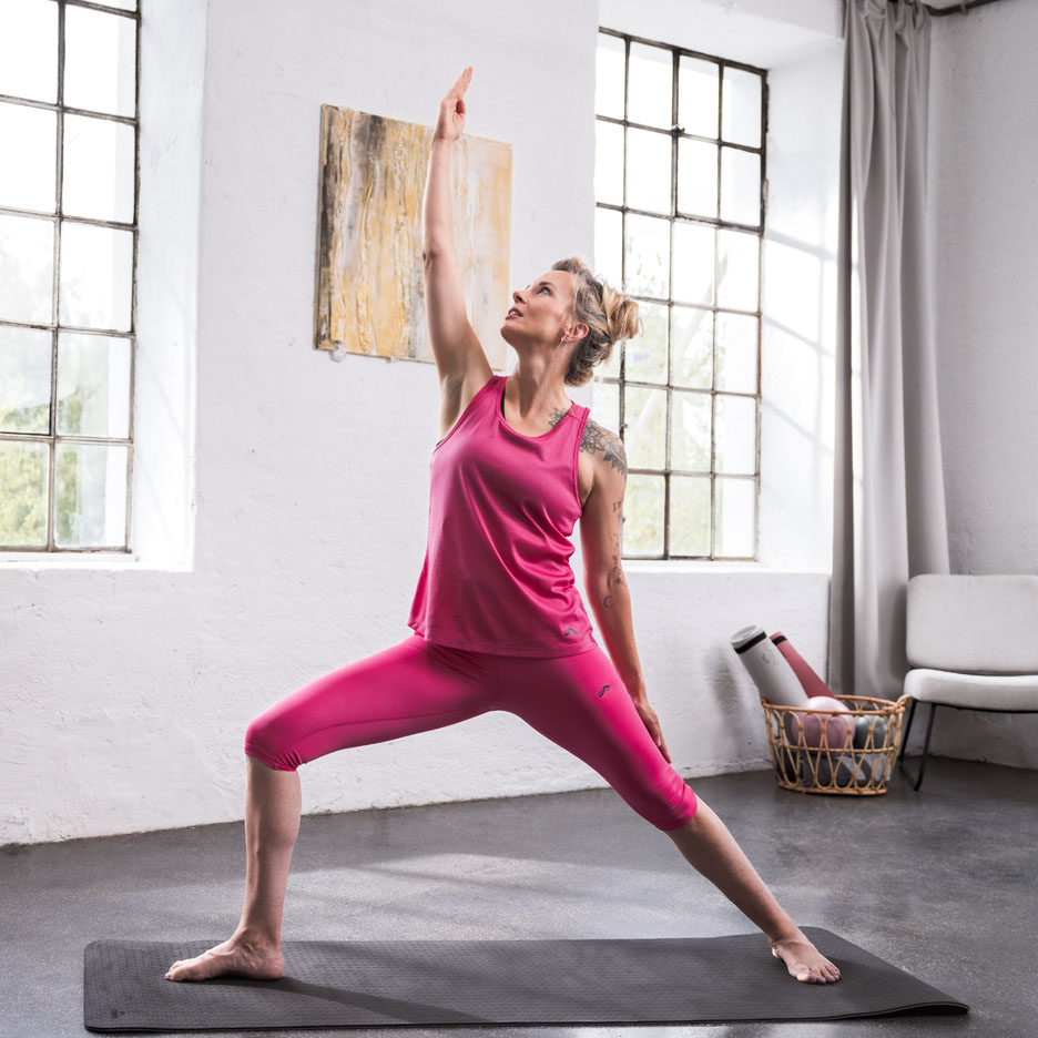 Femeie făcând yoga, purtând echipament sportiv roz într-o cameră luminoasă.