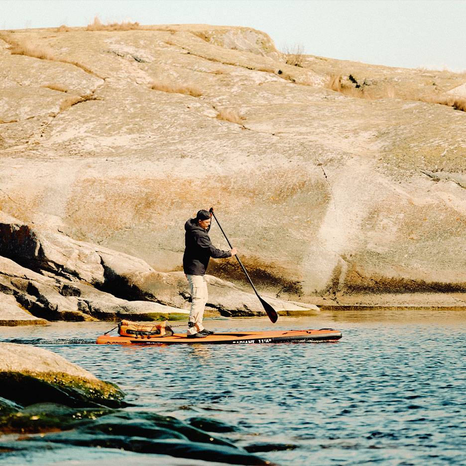 Bărbat vâslind pe o placă de paddleboard portocalie pe un lac stâncos.
