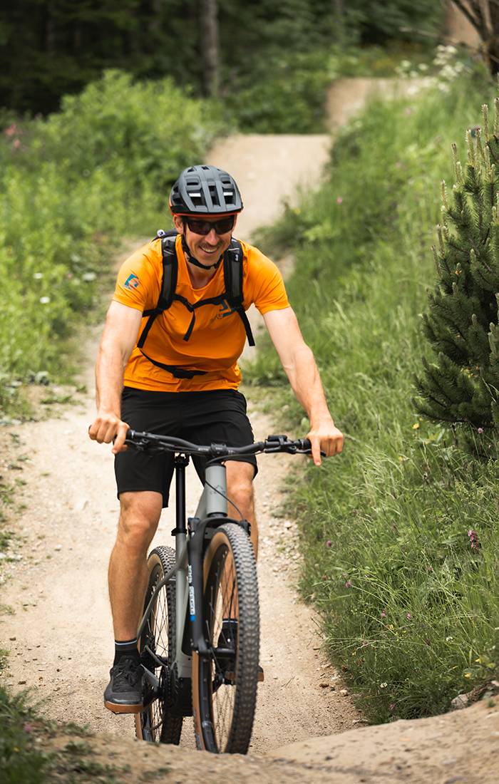 Un bărbat zâmbește în timp ce merge cu bicicleta de munte pe o potecă.