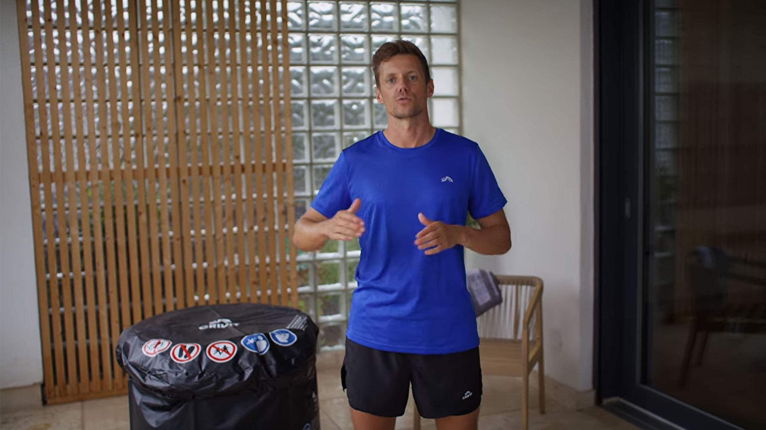 Bărbat în tricou albastru și pantaloni scurți negri, lângă o husă neagră pentru cadă cu hidromasaj.