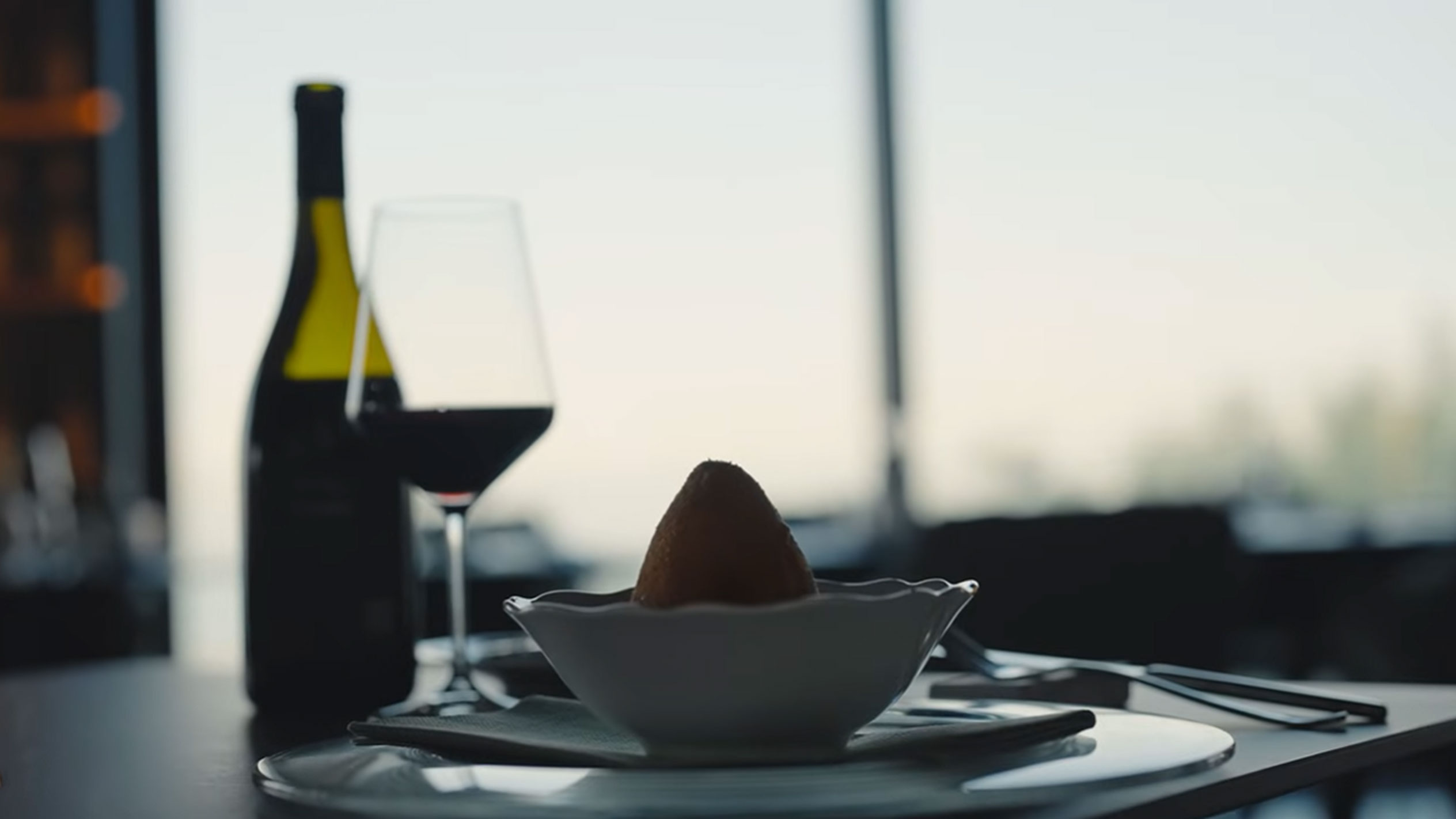 O sticlă de vin roșu și un pahar lângă un arancino într-un bol pe o masă.