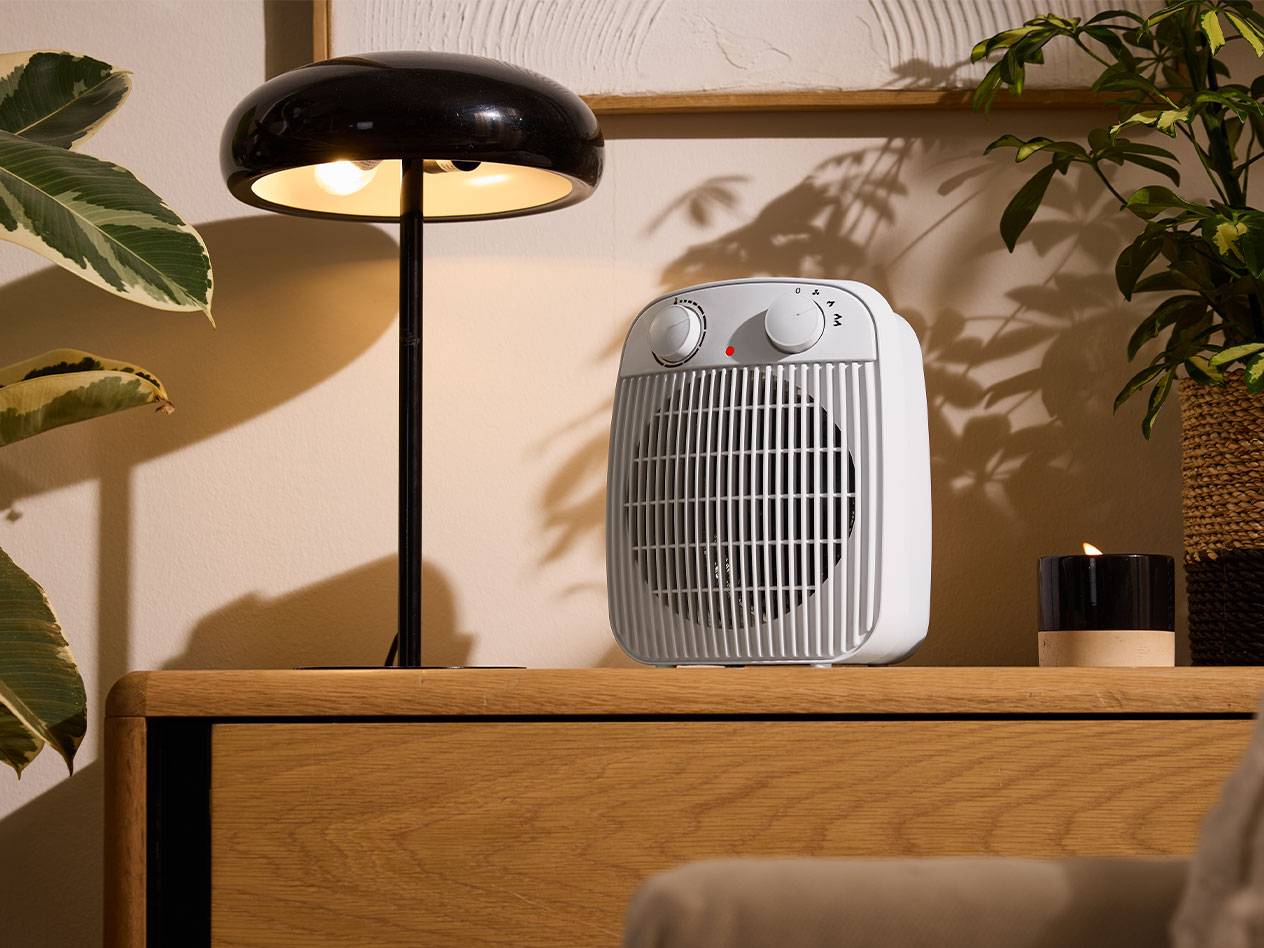 Aerotermă albă și lampă de masă neagră pe o piesă de mobilier din lemn într-o cameră confortabilă.
