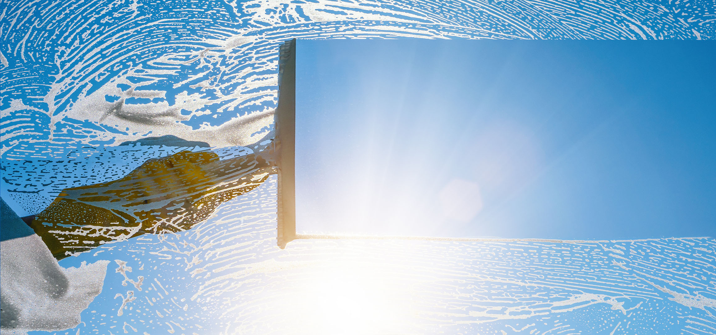 Curățarea ferestrelor cu spumă de săpun pe un cer albastru.