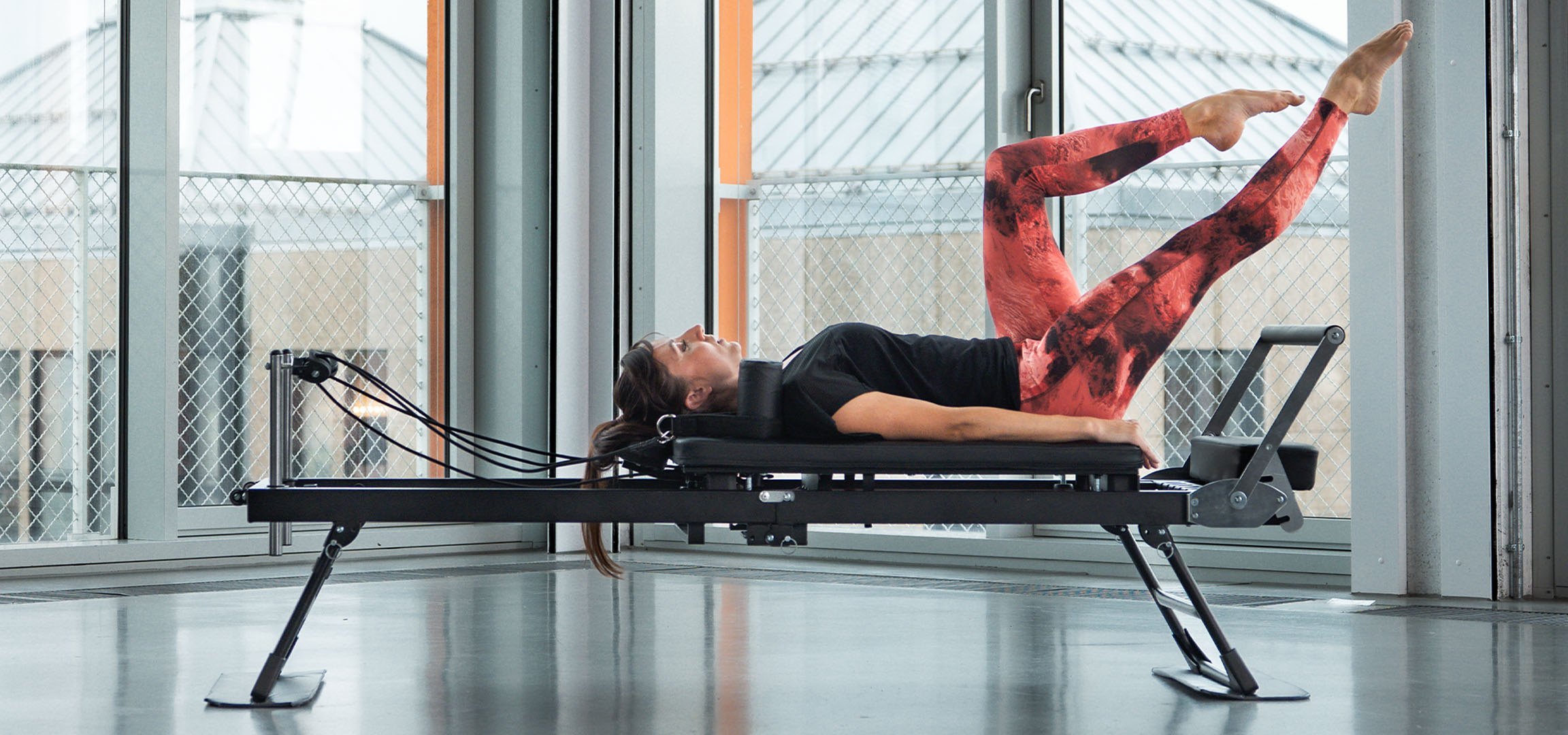 Femeie făcând Pilates pe un aparat reformer, cu accesorii de fitness în apropiere.