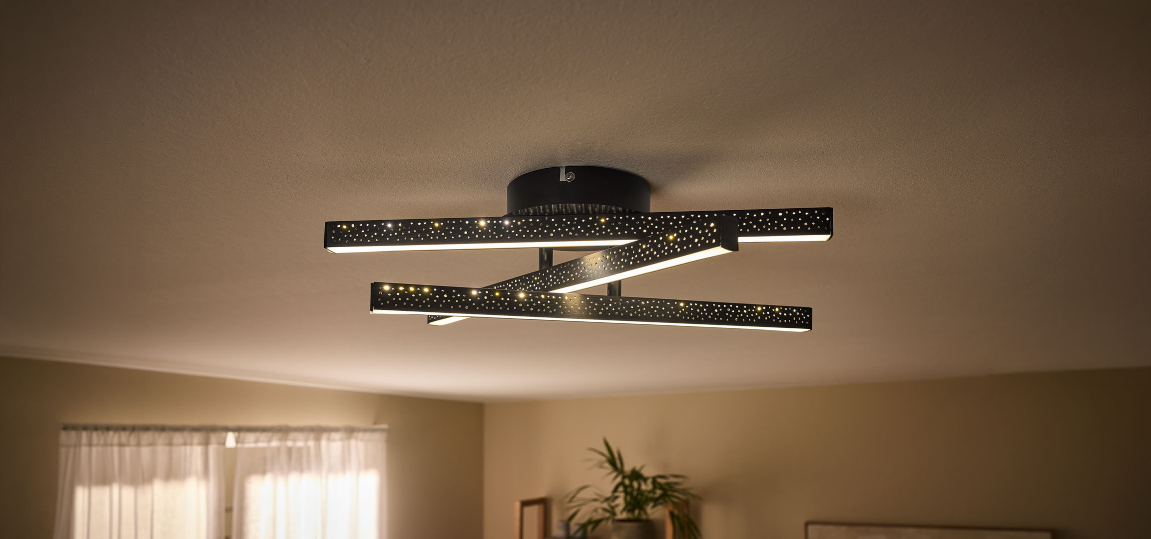 Plafonieră LED modernă cu bare negre perforate și lumină caldă.