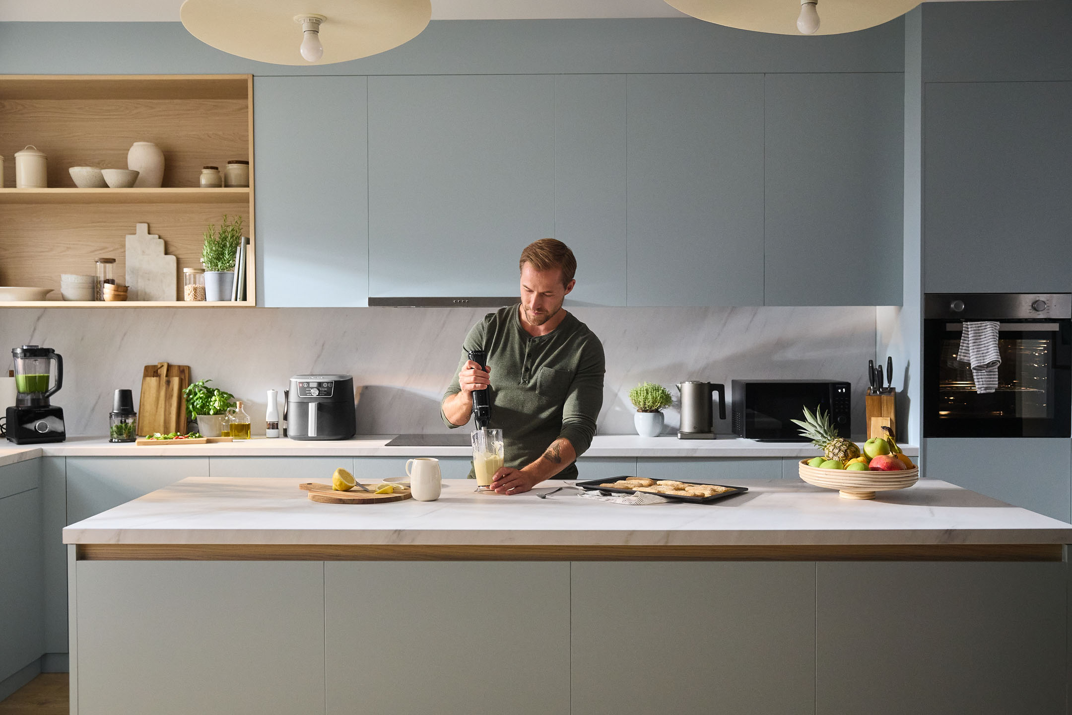 Bărbat folosind un blender vertical într-o bucătărie modernă cu aparate și fructe.