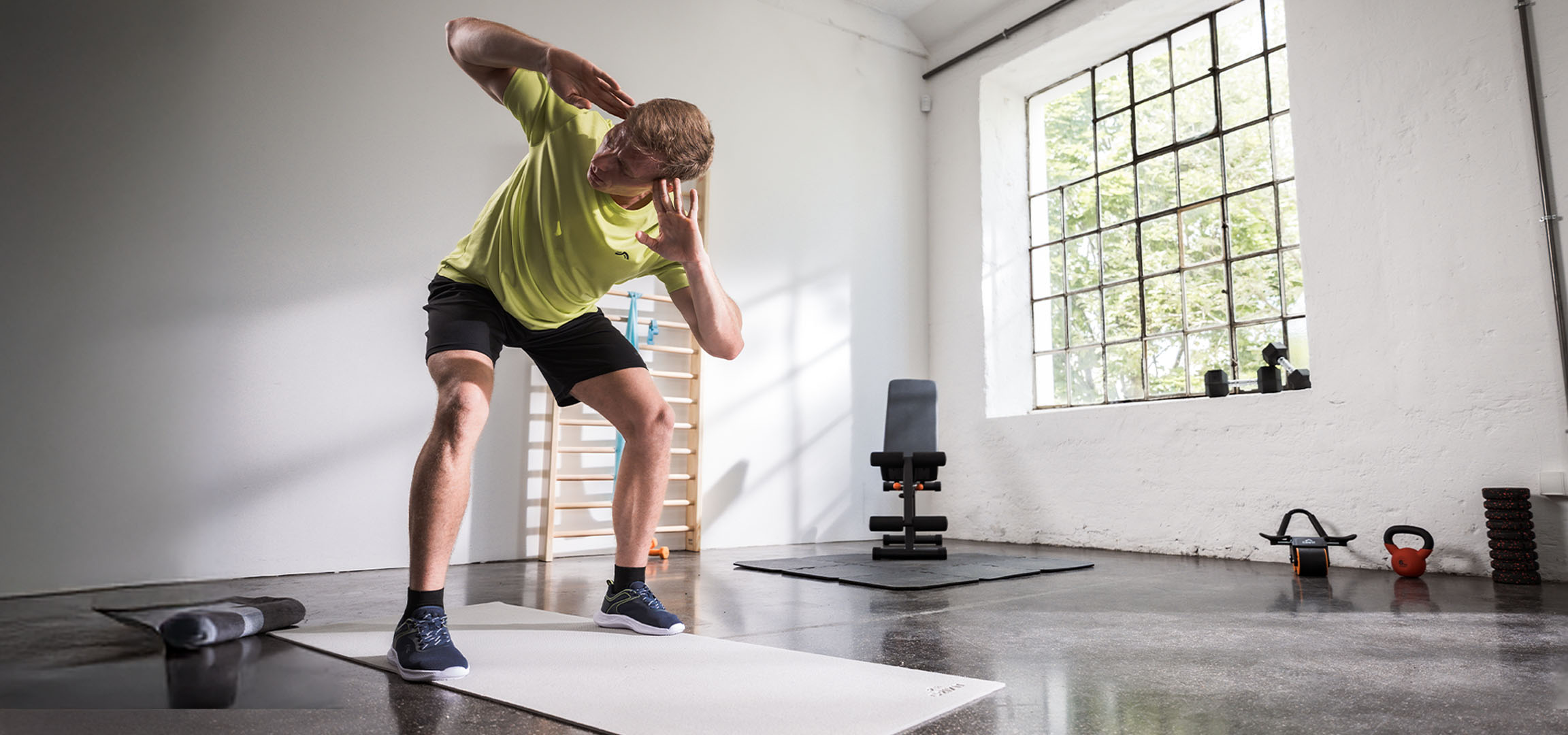 Bărbat care face exerciții într-o sală de sport, folosind un covor de yoga și gantere.