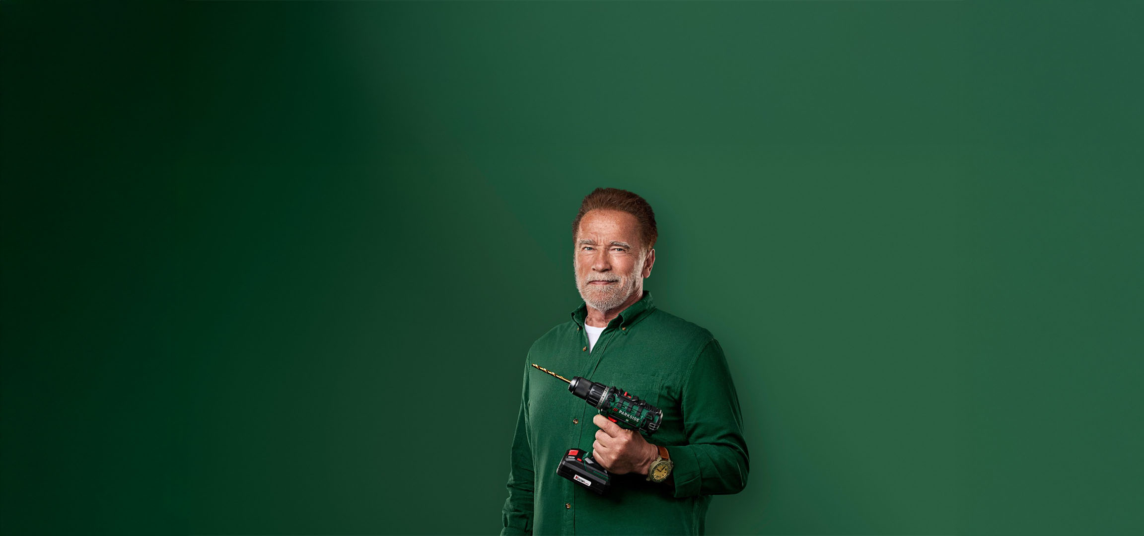 Arnold Schwarzenegger ținând o bormașină Parkside pe un fundal verde.
