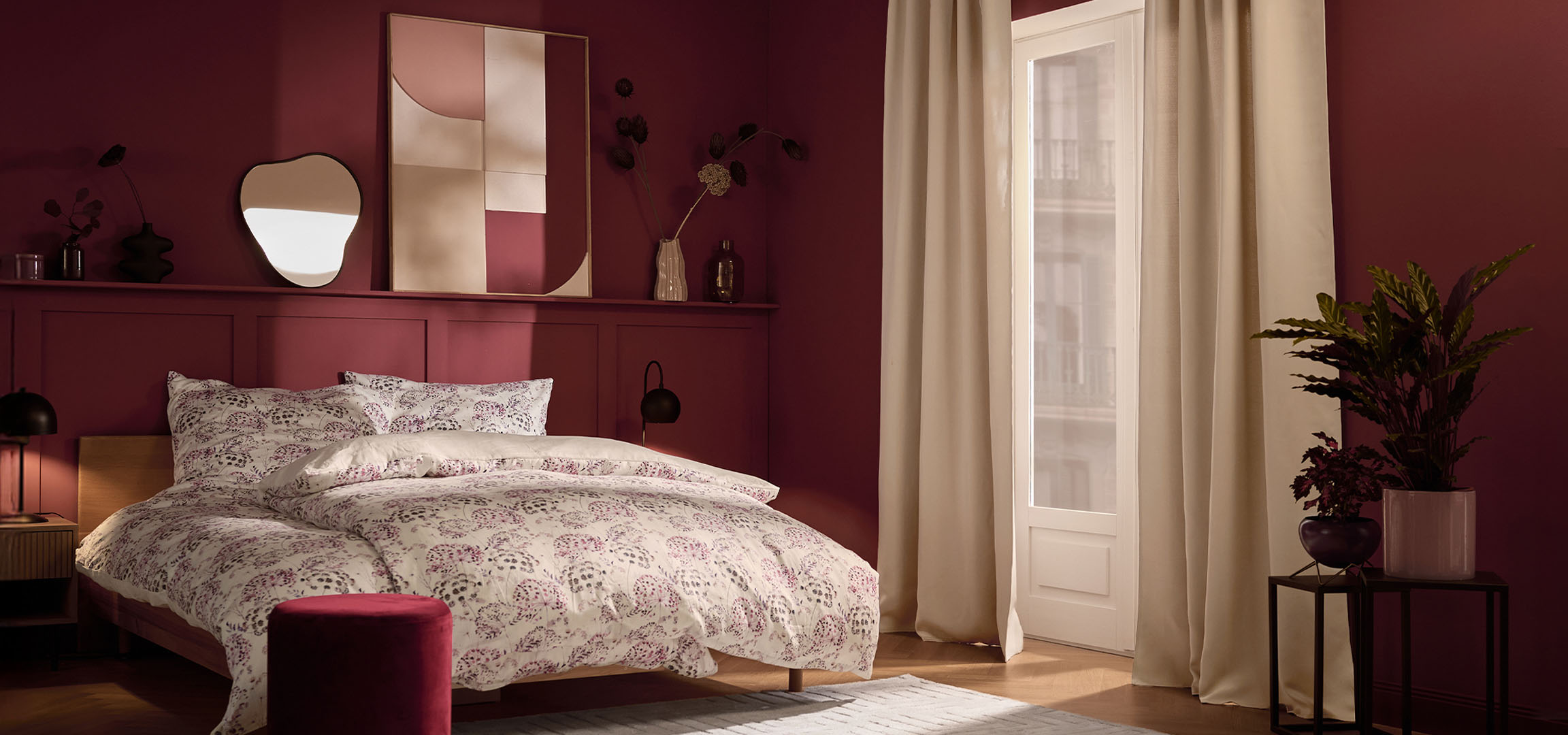 Dormitor cu pereți vișinii, pat cu lenjerie de pat albă cu model floral și plante.