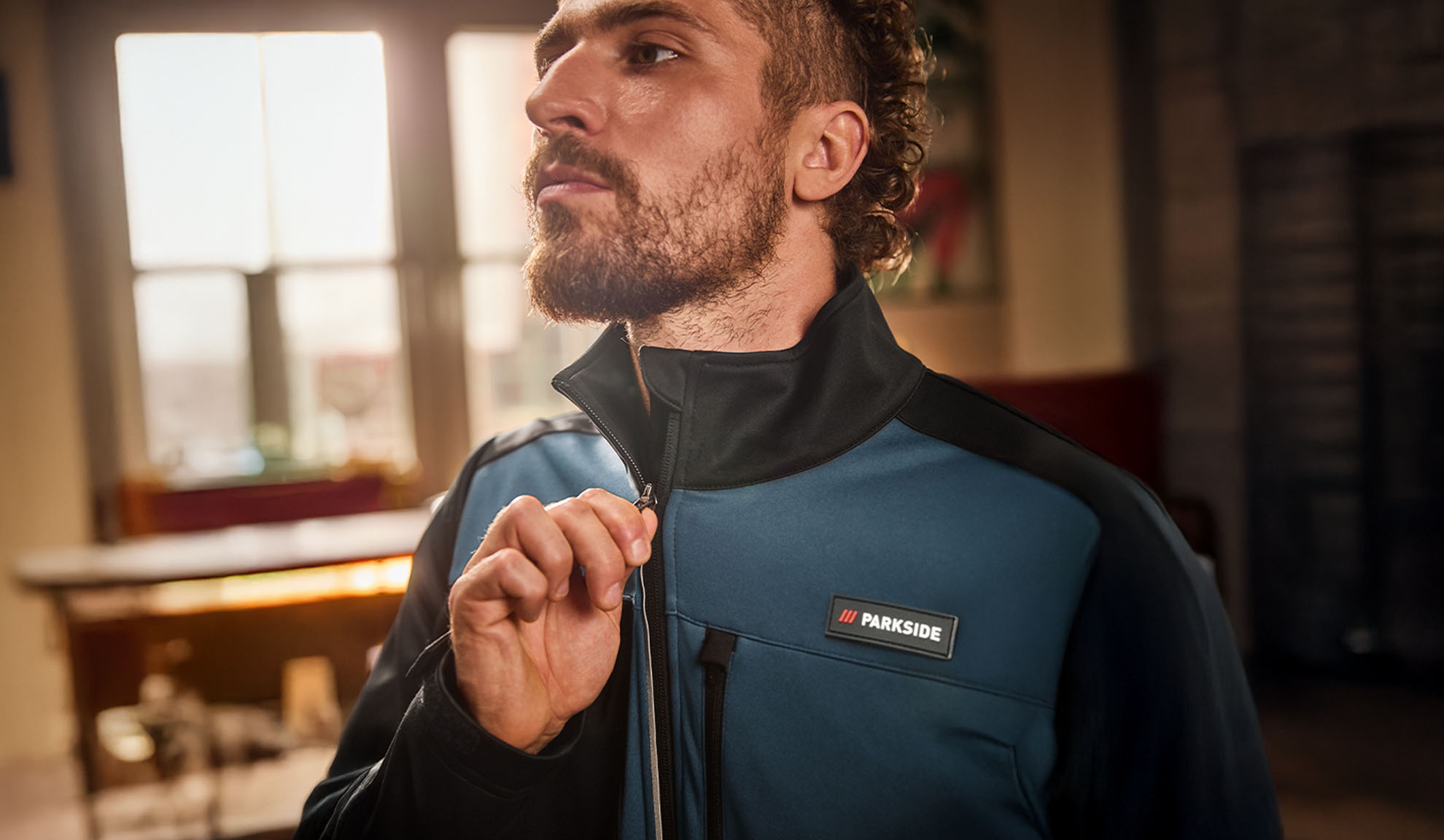 Bărbat într-o jachetă de lucru Parkside albastră și neagră, închizând-o cu fermoar.