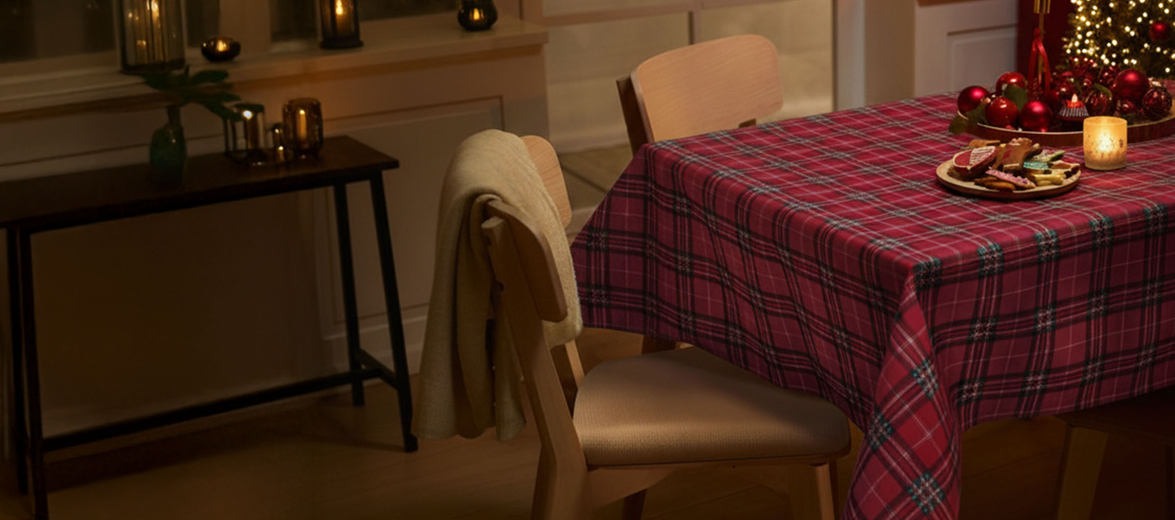 Aranjament de masă de Crăciun cu față de masă roșie în carouri, scaune și prăjituri de Crăciun.