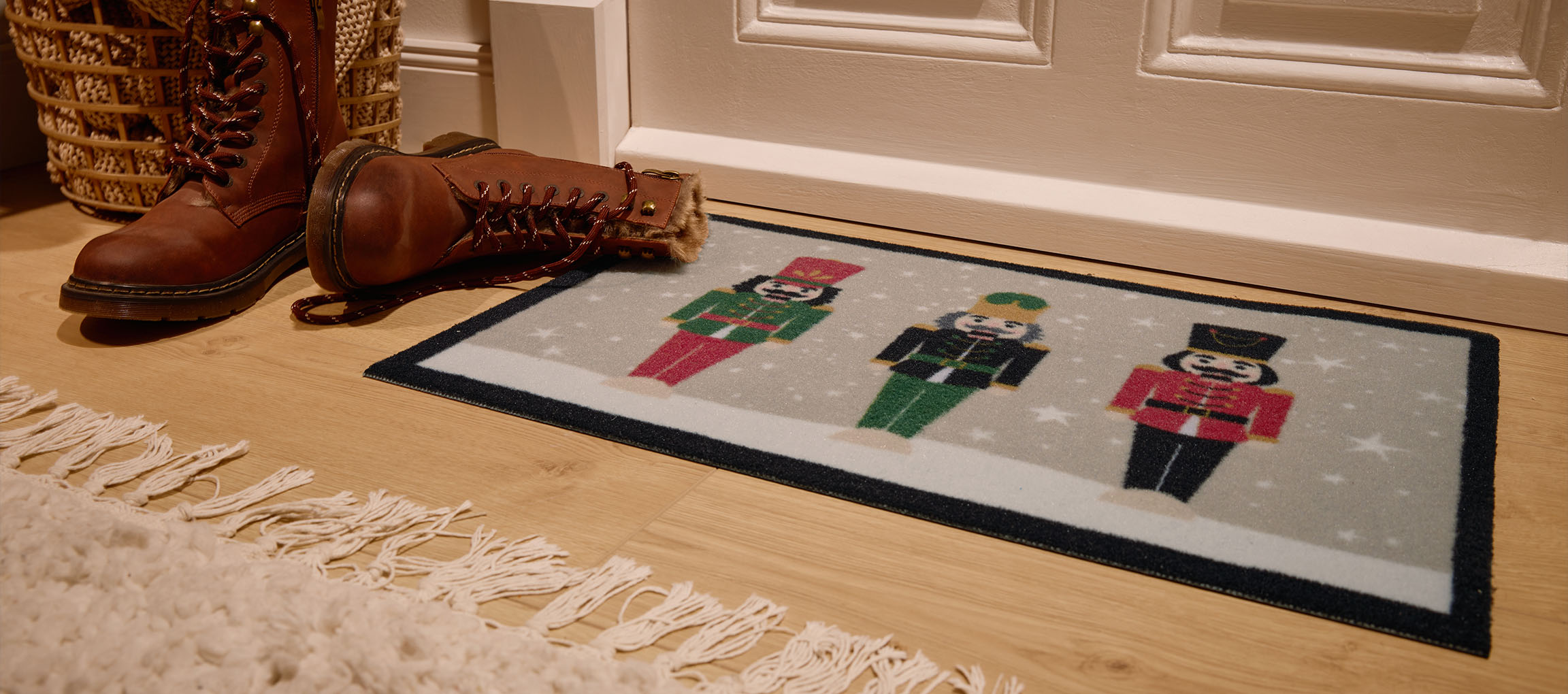 Covoraș de Crăciun cu spărgătoare de nuci, cizme maro și coș de răchită la intrare.