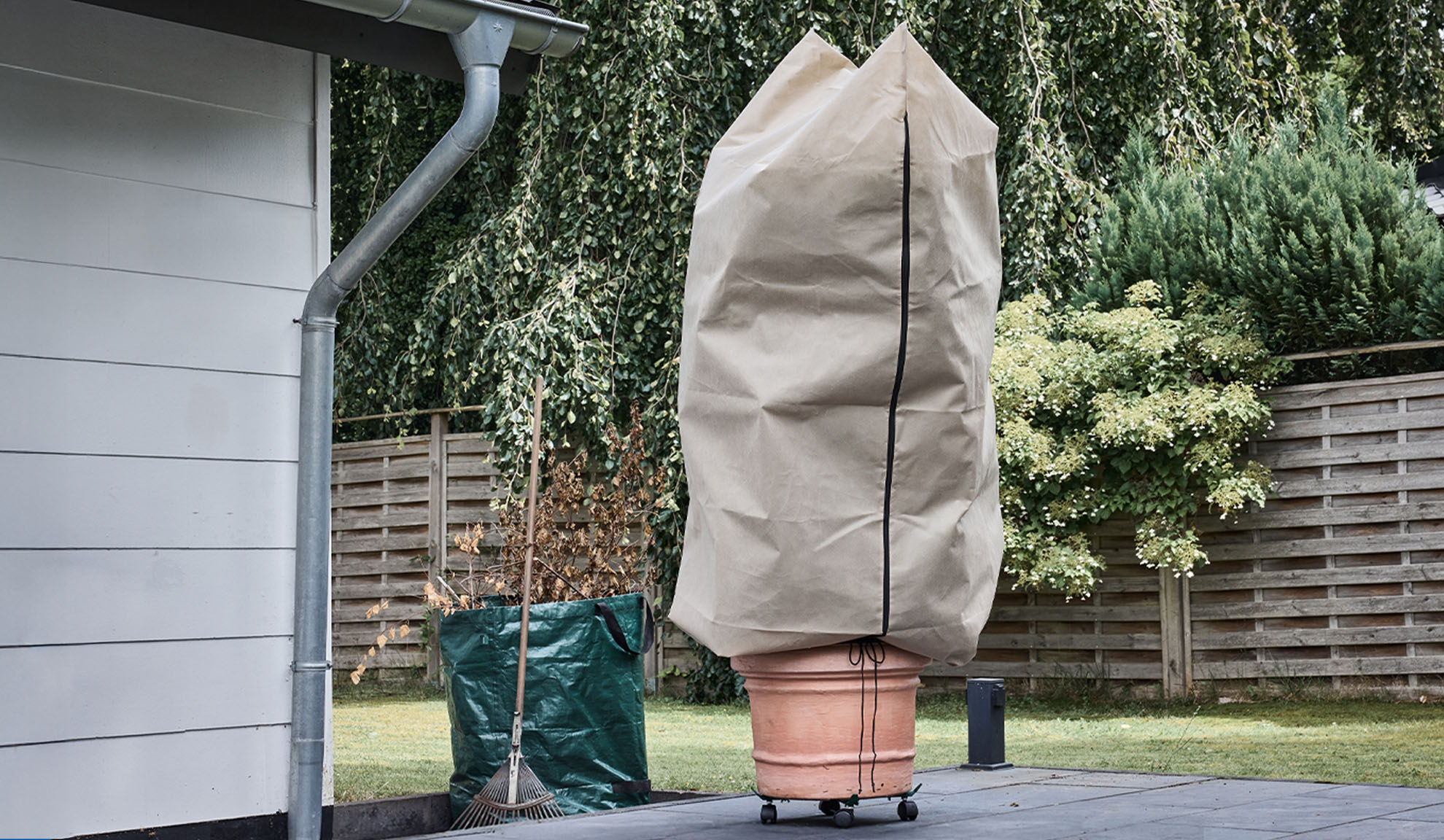 Husă pentru plantă în ghiveci pe o terasă cu jgheab și greblă.