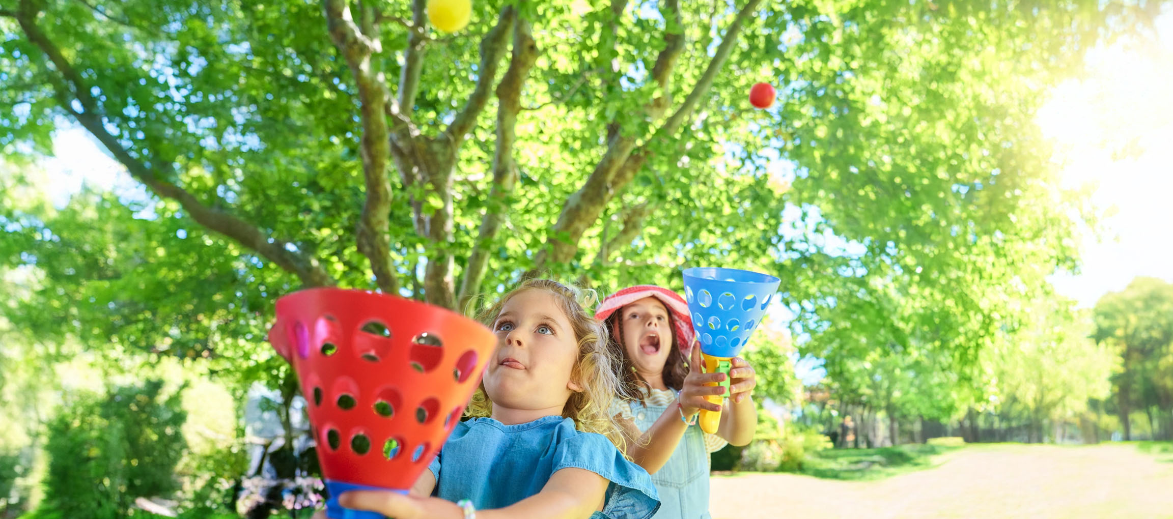 Două fete se joacă cu mingi într-un parc însorit.