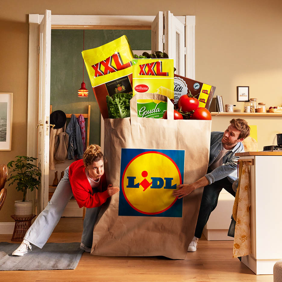 Un cuplu se chinuie să împingă o pungă de cumpărături Lidl supradimensionată, plină cu produse XXL.