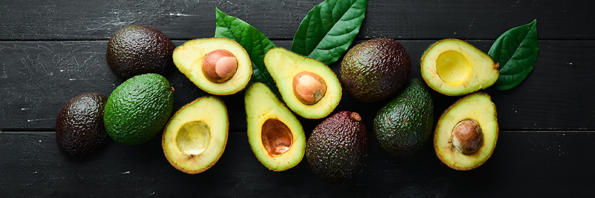 Avocado, tăiate și întregi, pe o suprafață de lemn negru.