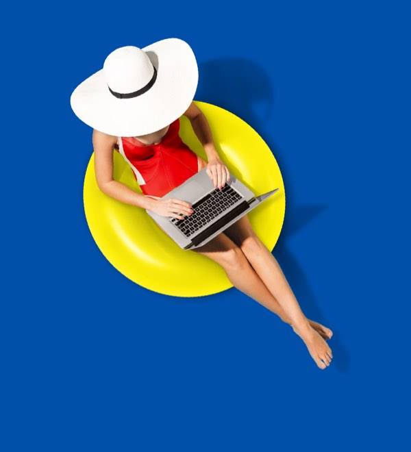 O femeie în costum de baie roșu și pălărie albă lucrează la laptop pe un colac galben.