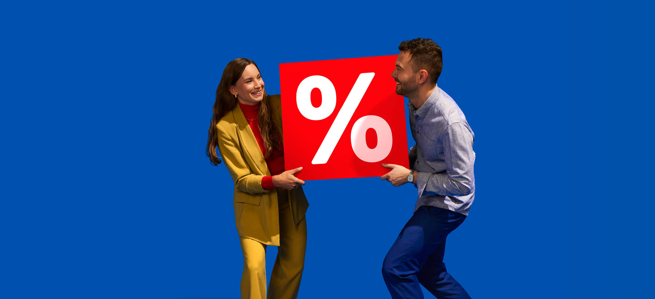 Doi oameni zâmbitori țin o pancartă roșie mare cu simbolul procentului.