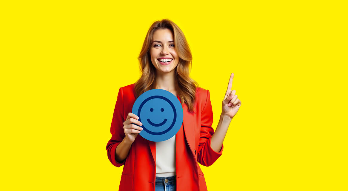 Femeie zâmbitoare într-un sacou roșu, ținând un emoticon albastru și arătând în sus.