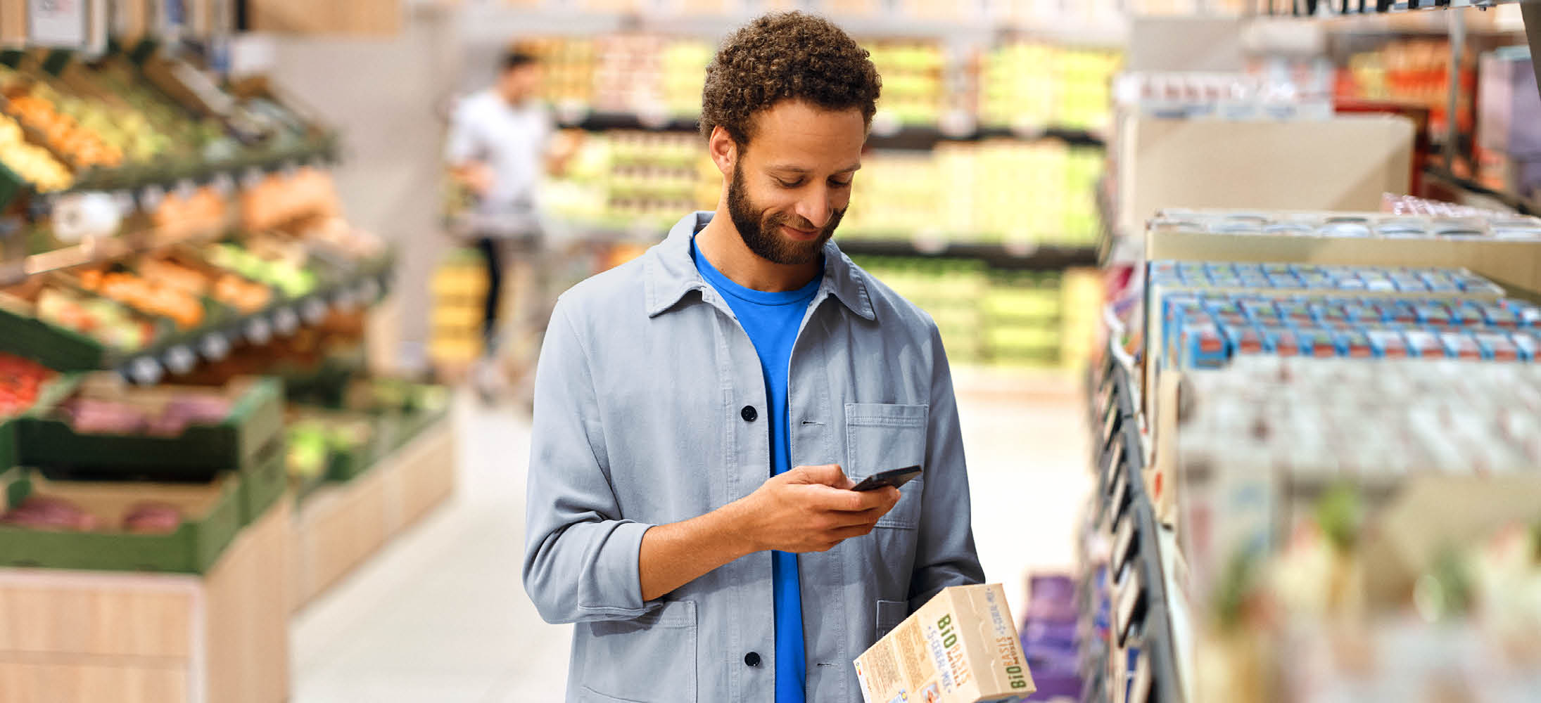 Bărbat într-un supermarket, scanând un produs alimentar ecologic cu telefonul.