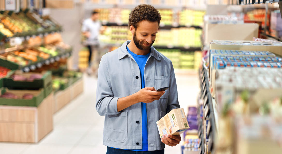 Bărbat într-un supermarket, scanând un produs alimentar ecologic cu telefonul.