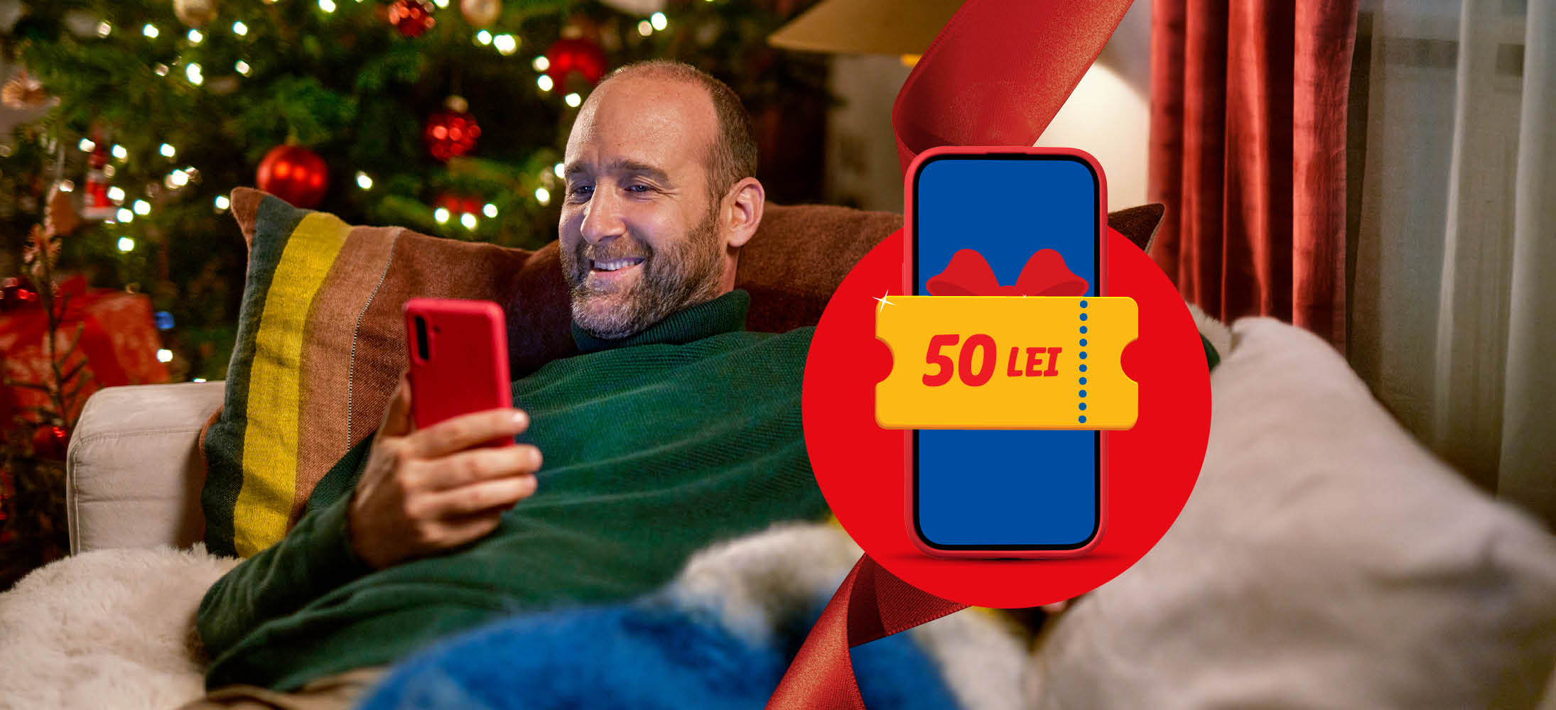 Bărbat zâmbitor pe canapea, cu telefonul în mână, lângă un brad de Crăciun, cu un voucher de 50 LEI.