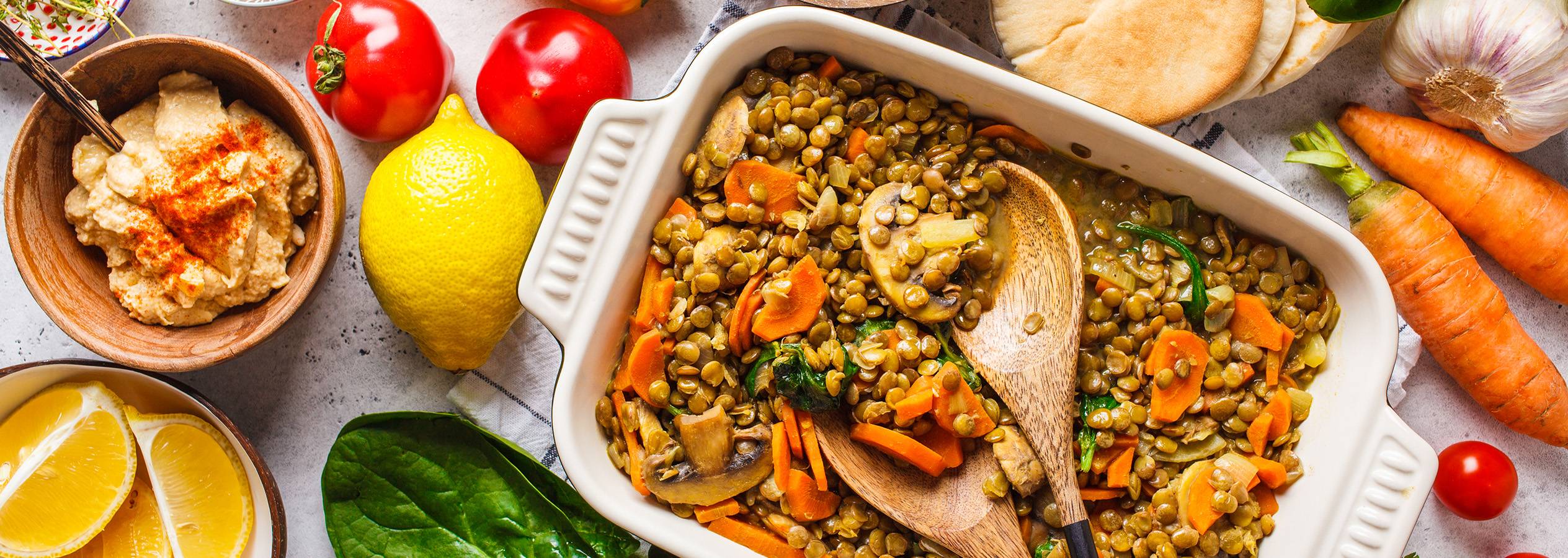 O tavă cu linte gătită cu legume, servită cu hummus și pâine pita.