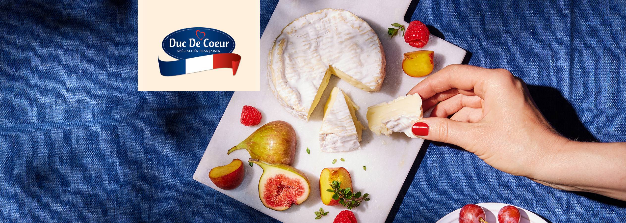 Brânză Duc De Coeur cu fructe pe o masă albastră.