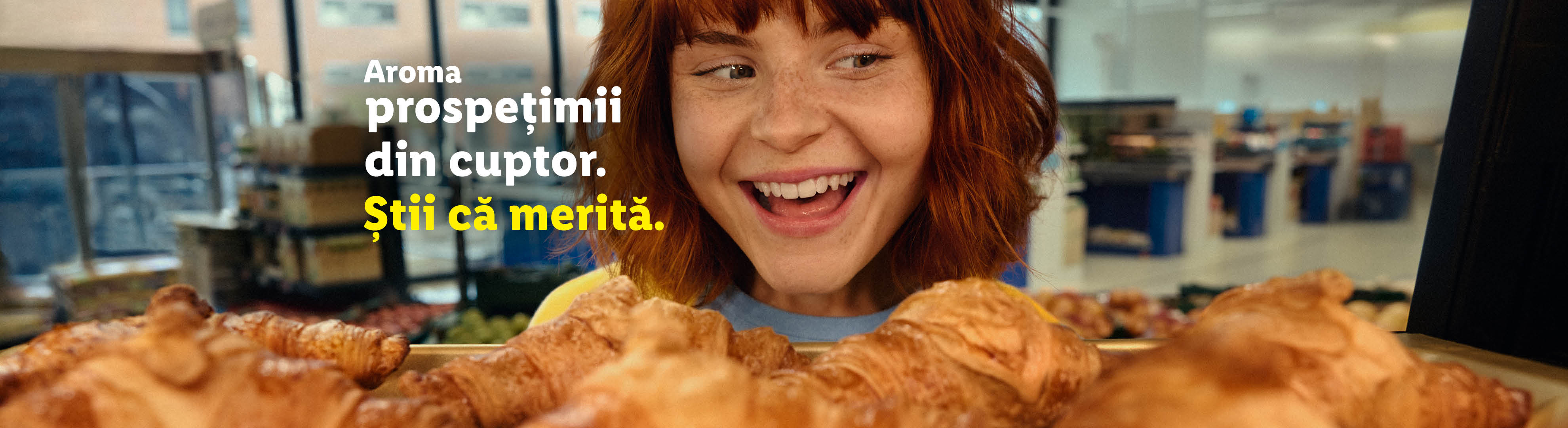 O femeie zâmbitoare privește croissante proaspete, cu textul „Aroma prospețimii din cuptor. Știi că merită.”