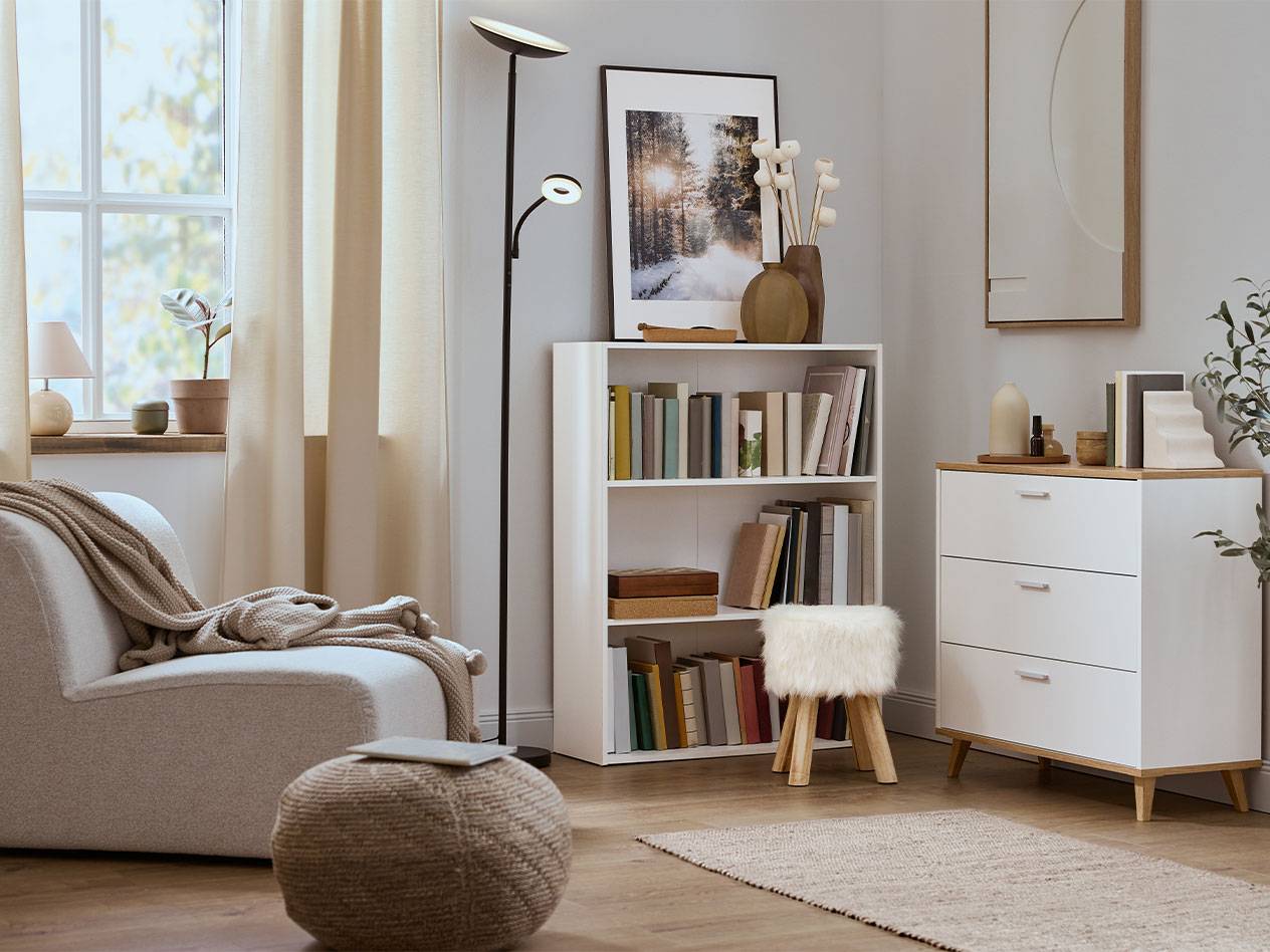 Living confortabil cu fotoliu, bibliotecă și comodă în culori neutre.