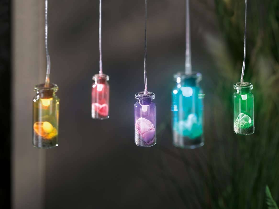 Cinci luminițe decorative în formă de borcănașe mici, cu pietricele colorate în interior, atârnă de fire subțiri.