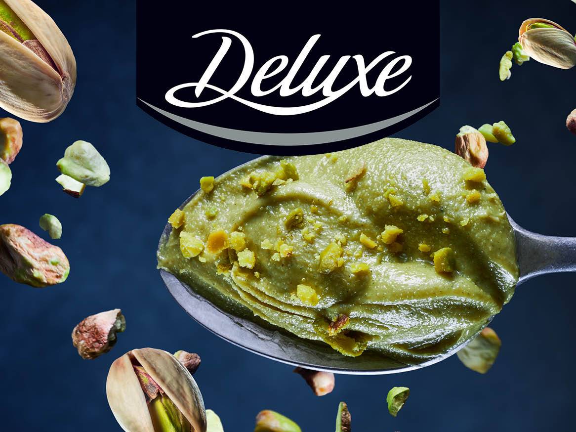 Înghețată de fistic Deluxe pe o lingură, cu fisticuri plutind în jur.