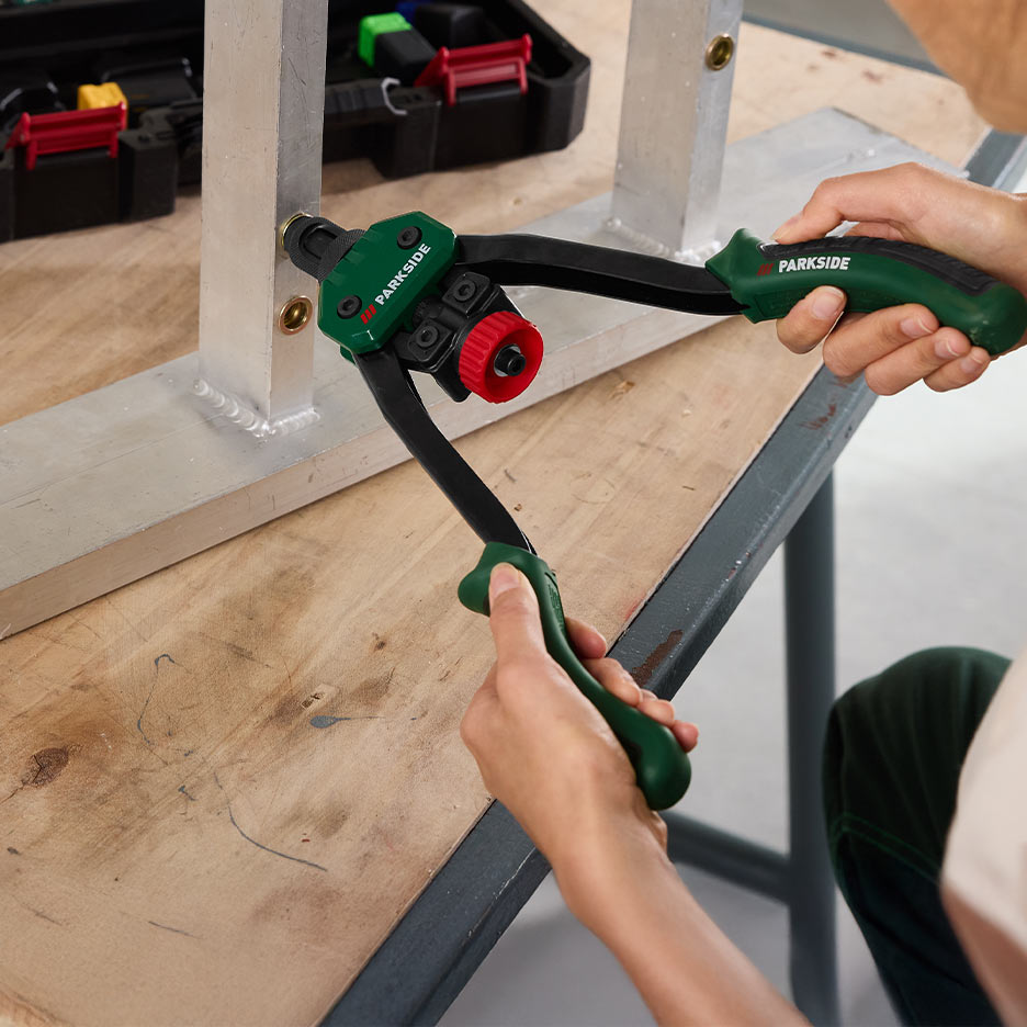 O persoană folosește un clește de nituit Parkside pentru a fixa o nituire într-o piesă metalică.