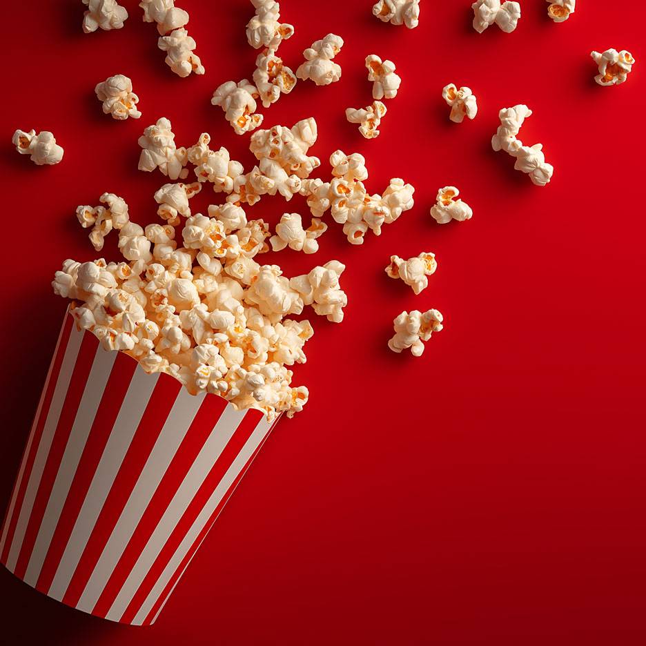 Popcorn pe fundal roșu, o parte din popcorn într-o cutie de carton dungată.