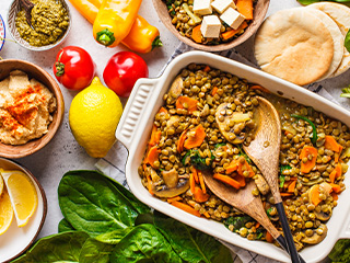 O tavă cu linte, ciuperci și legume, alături de humus, pâine pita și alte ingrediente proaspete.